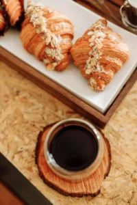 Almond croissants served on a wooden tray with a cup of black coffee.