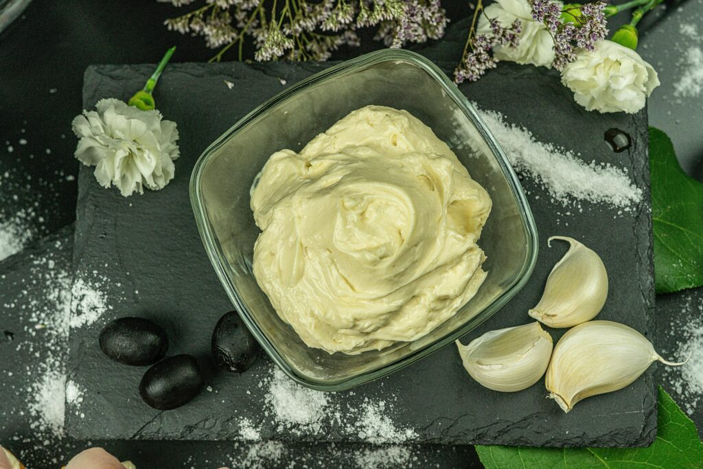 garlic aioli in a bowl plus three gloves of garlic and olives