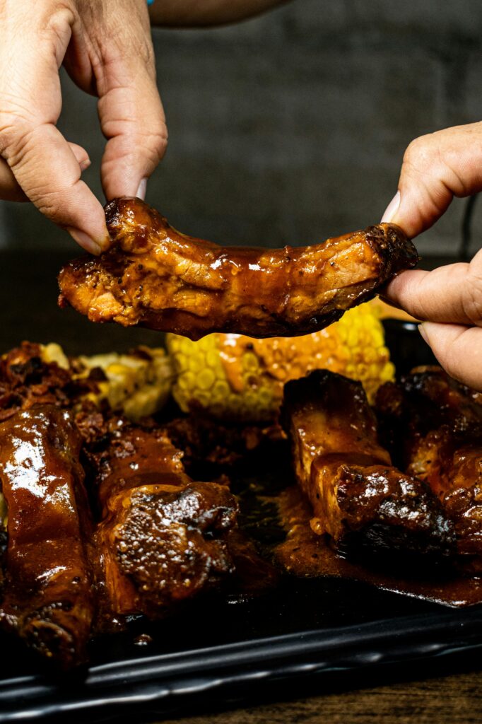 two hands showing a short rib. behind there are other already cooked ribs