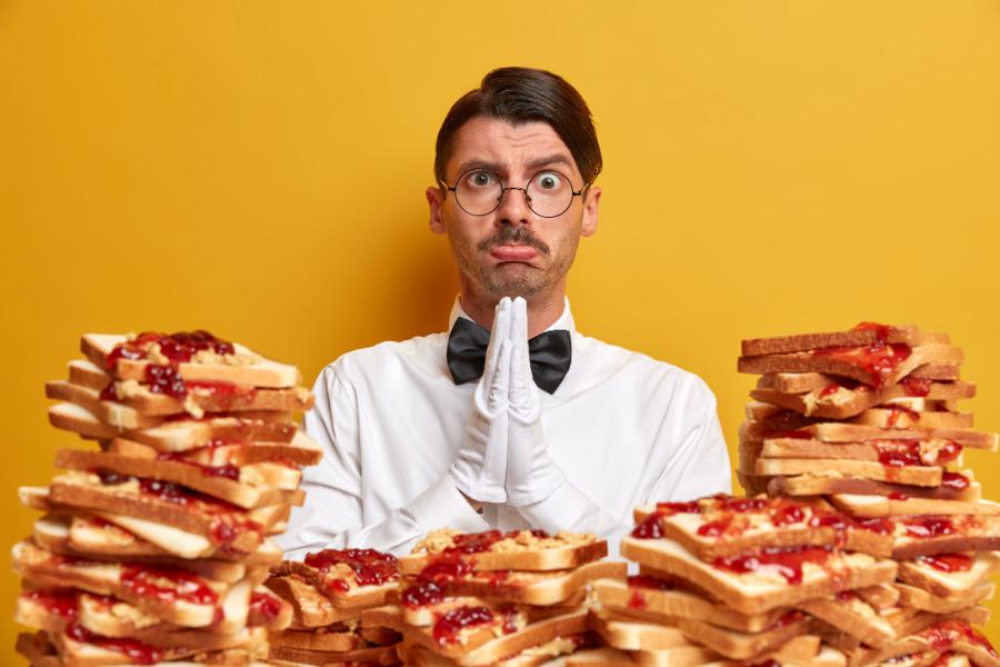 sad-waiter surrounded-by-pile-bread-snacks-poses-against-yellow-wall