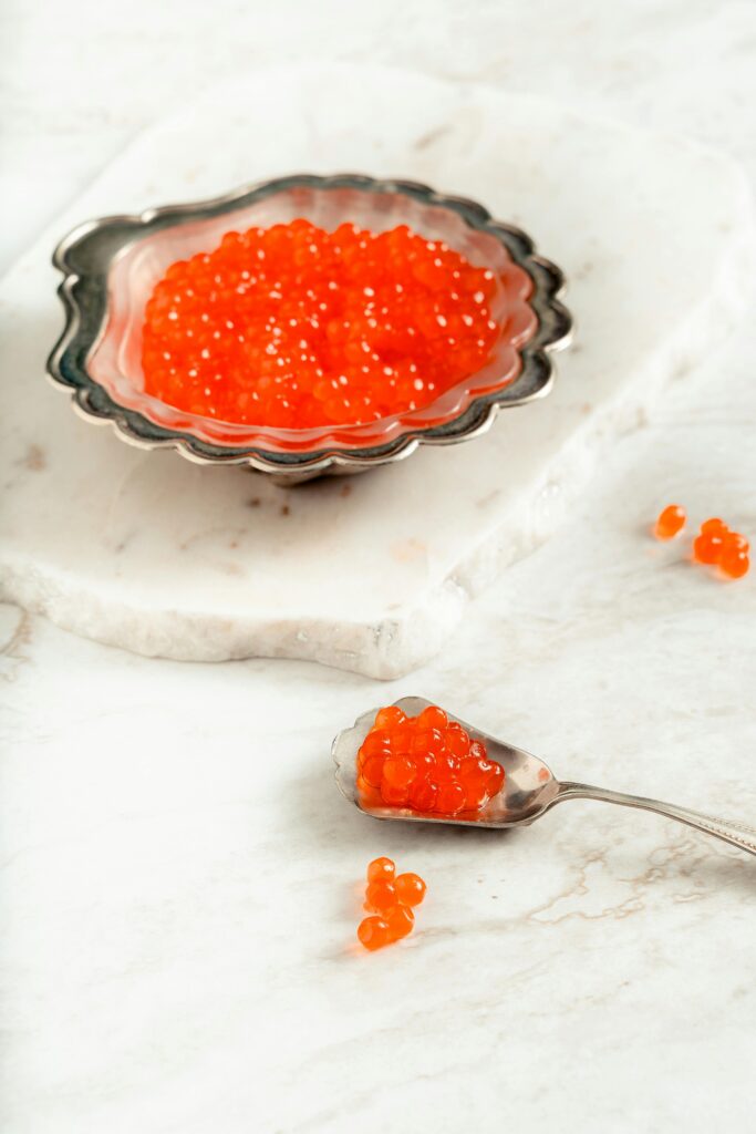 A High Edged Plate Full of Caviar on Marble Beside a Spoon Full of Caviar