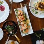 An elegant spread of dishes on a wooden table, featuring lemon herb grilled shrimp garnished with microgreens, roasted vegetables, and other gourmet accompaniments.