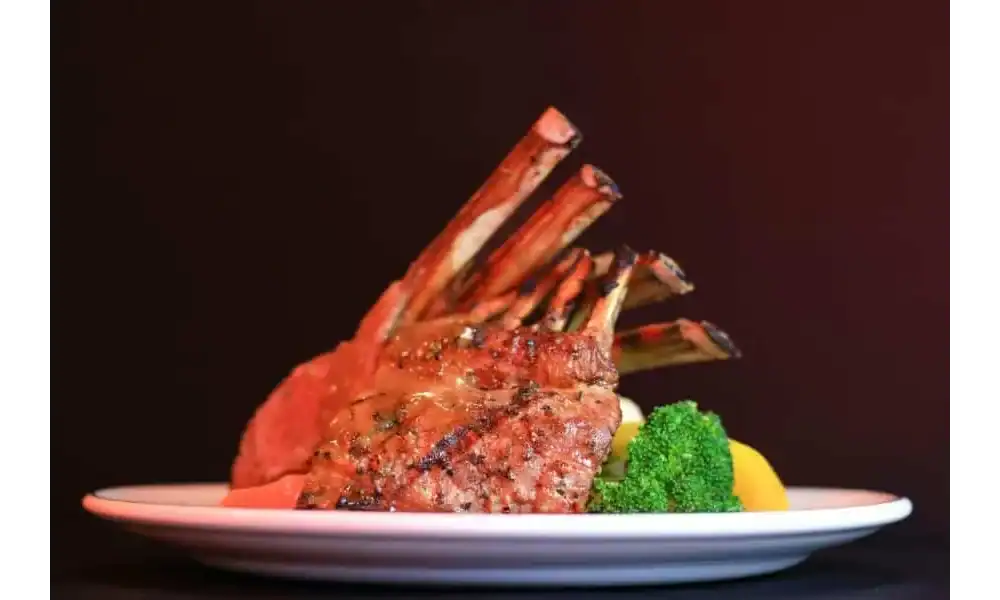 Grilled herb-crusted rack of lamb served on a white plate with broccoli and lemon