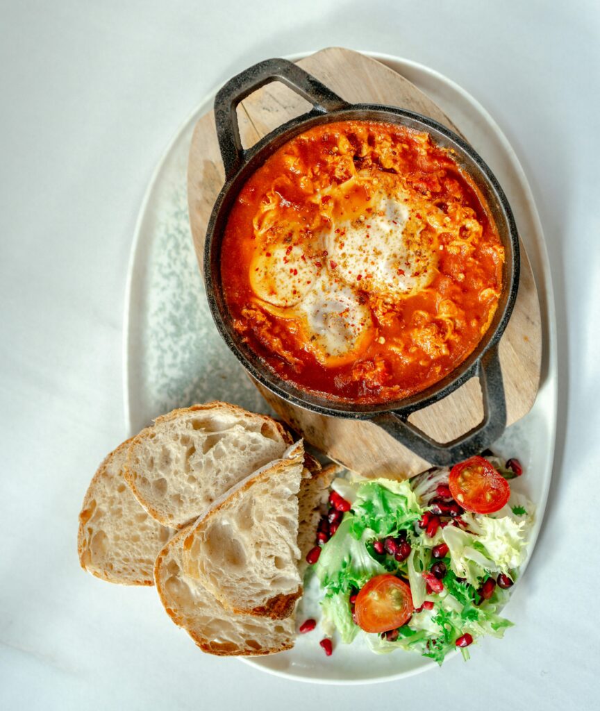 Shukshuka in a Pan and Slices of Bread and Salad