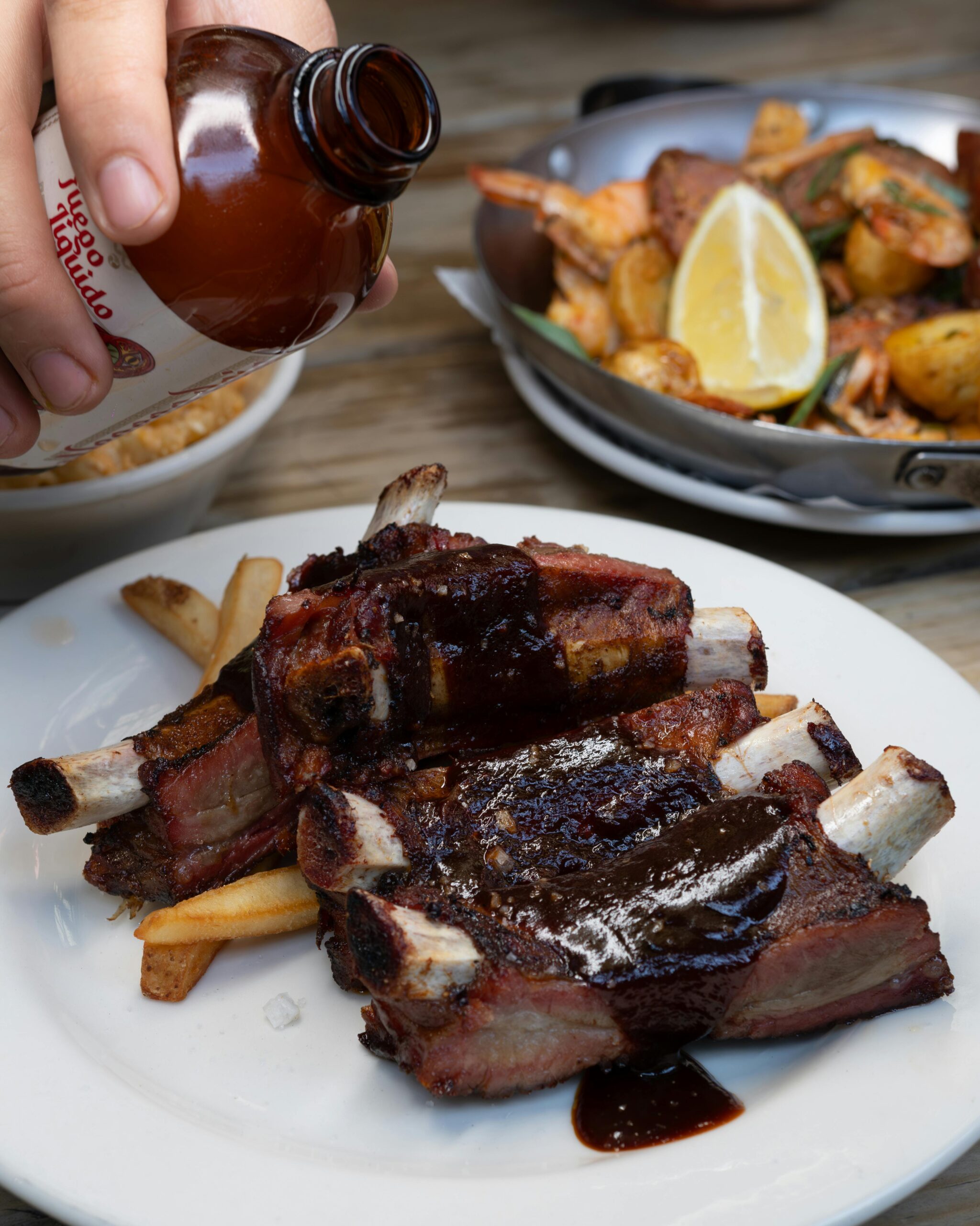 ribs shor ribs served in a white plate behind there are potatoes and a slice of lemon