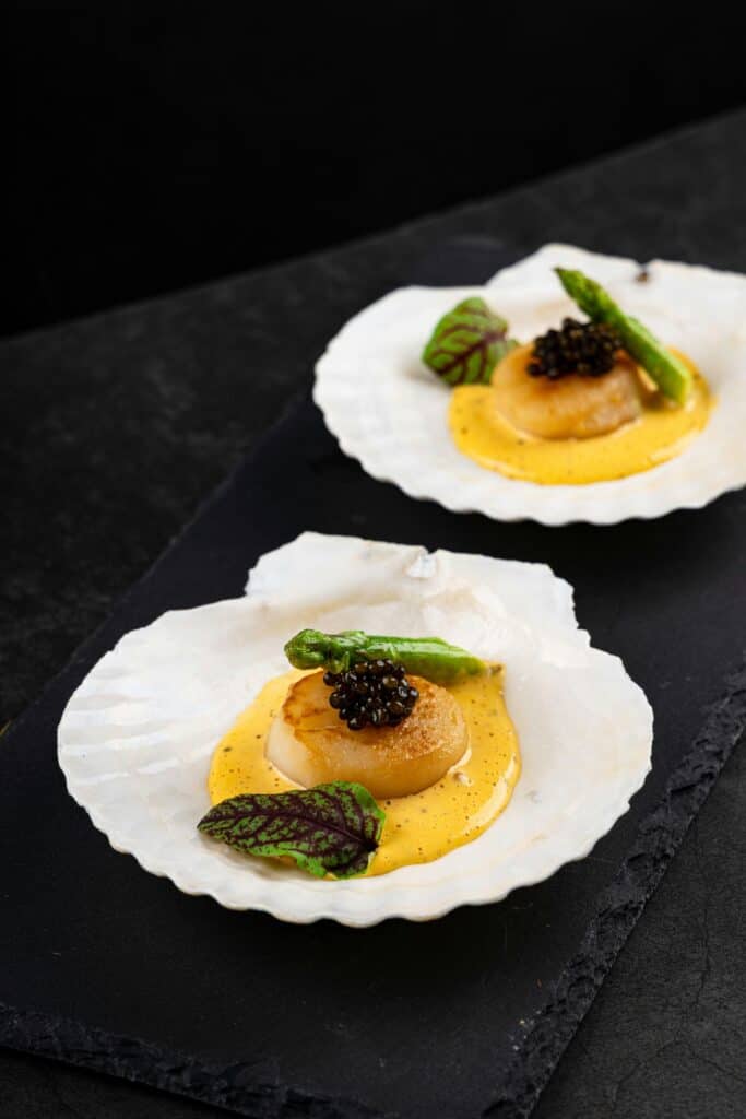 two plates of scallops on lemon butter garnished with asparagus
