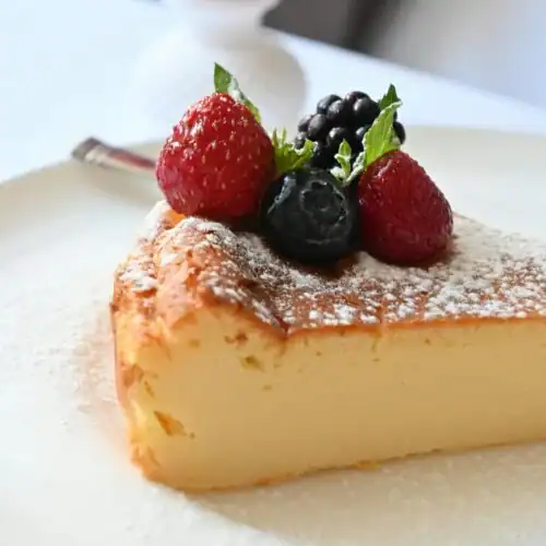 A slice of French toast soufflé topped with powdered sugar and fresh berries on a white plate.
