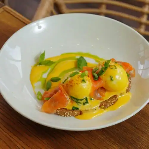 Smoked salmon benedict topped with poached eggs, hollandaise sauce, and garnished with fresh scallions and herbs.