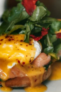 Smoked salmon benedict topped with creamy hollandaise foam, fresh greens, and red pepper flakes for garnish.