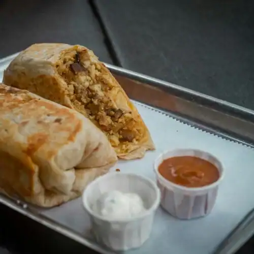 A sliced chicken Mexican breakfast burrito served on a metal tray, accompanied by sour cream and salsa in small cups.