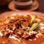 A plate of authentic Mexican chilaquiles topped with crumbled chorizo, sliced avocado, onions, crema, and cheese.