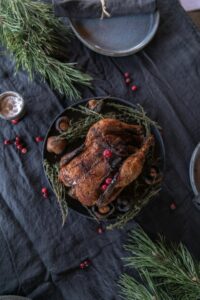 Roasted chicken garnished with herbs and berries with a dark background