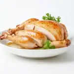 A perfectly roasted whole chicken, golden and juicy, sliced to reveal tender meat, garnished with fresh parsley and served on a white plate.
