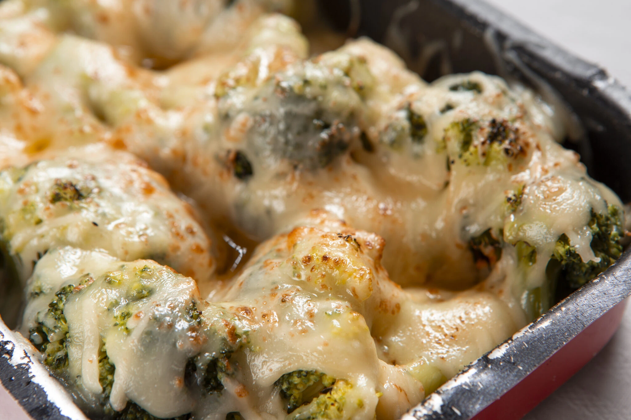 Broccoli chicken rice casserole topped with golden melted cheese in a red pan