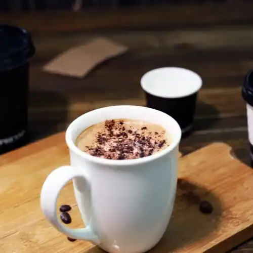 A warm cup of French hot chocolate in a white ceramic mug on a wooden tray, topped with a sprinkle of cocoa powder.