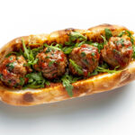 a meatball sub with sauce and greens