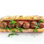 A lamb meatball sub in a crispy baguette, topped with tomato sauce, fresh arugula, and garnished with parsley.