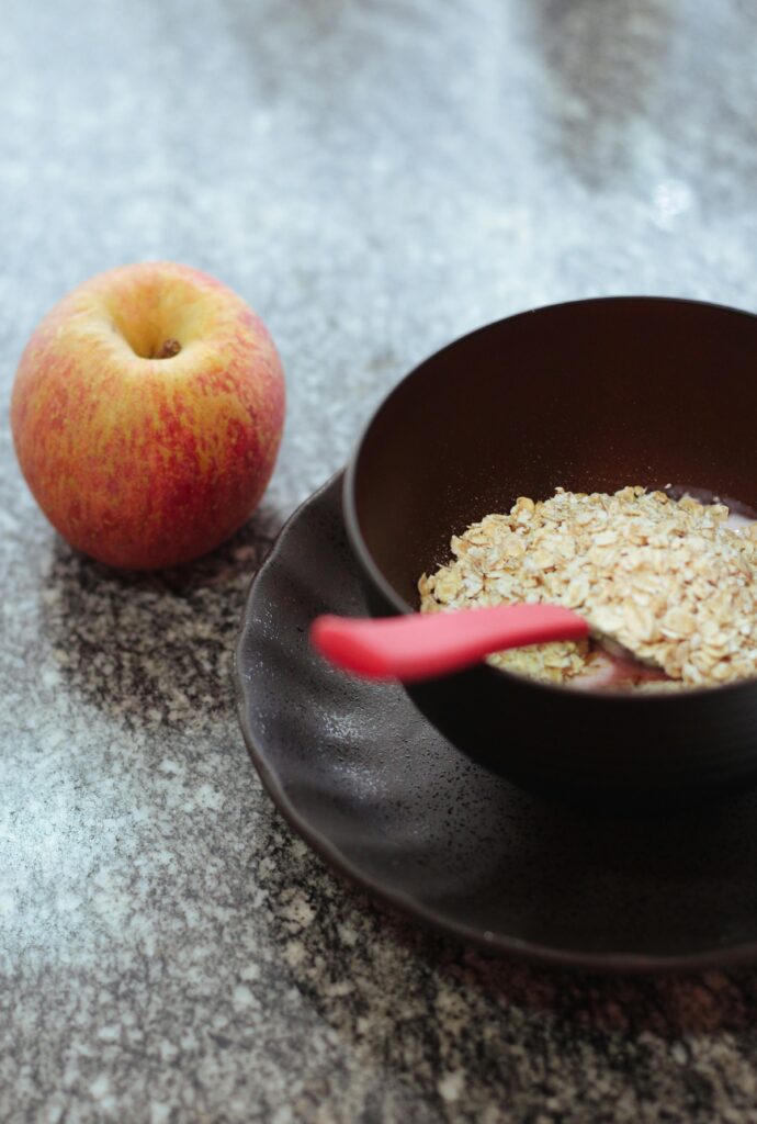 oatmean in a black bowl with a spoon and an apple along it 