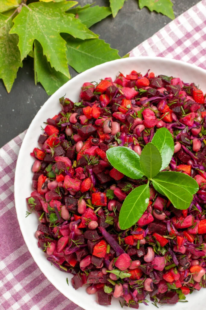 A vibrant beetroot salad with diced vegetables, fresh herbs, and leafy garnish, served in a white bowl on a checkered cloth with autumn leaves in the background.