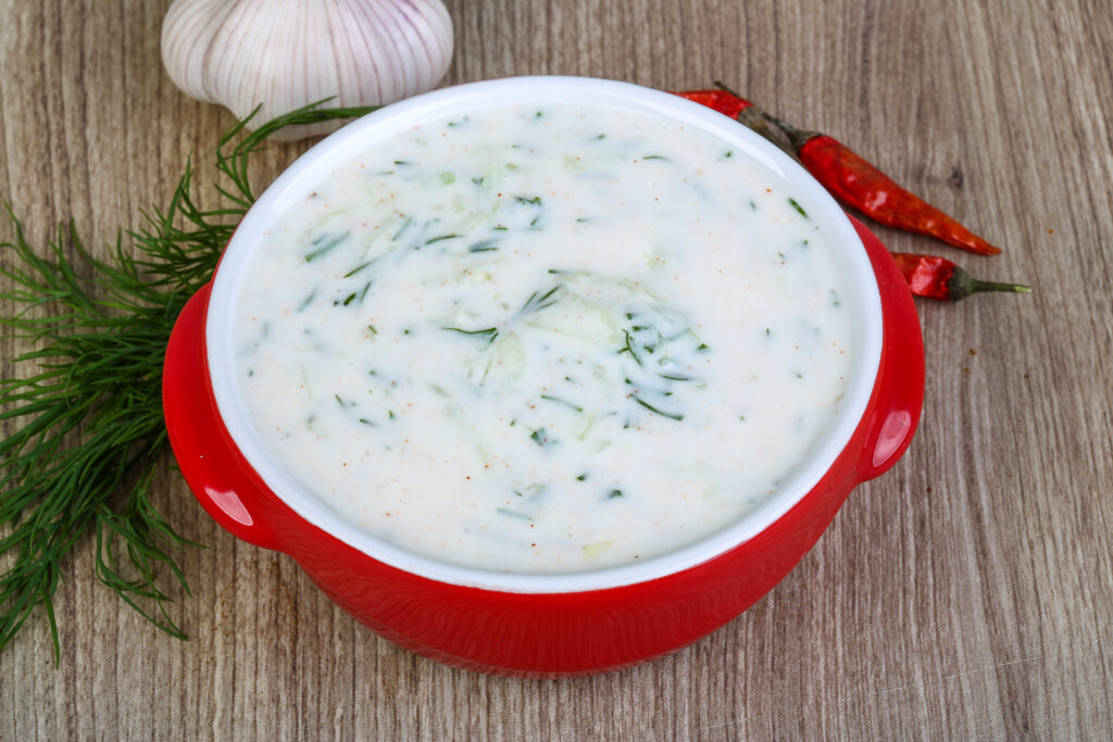 Tzatziki with cucumber and dill in a red bowl on wood