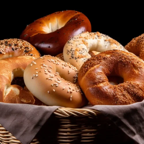 A basket filled with a variety of freshly baked bagels, including sesame, poppy seed, and plain, displayed on a dark background.