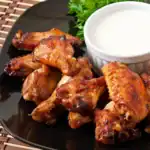 Juicy, golden-brown buffalo wings served on a black plate with a creamy dipping sauce and fresh parsley garnish.