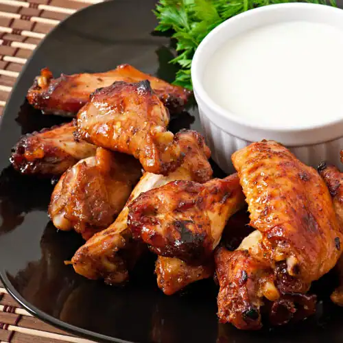 Juicy, golden-brown buffalo wings served on a black plate with a creamy dipping sauce and fresh parsley garnish.
