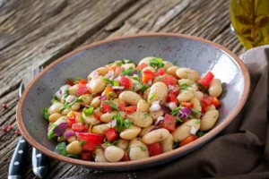 A colorful white bean salad with diced tomatoes, red onions, fresh herbs, and a drizzle of olive oil, served in a rustic ceramic bowl on a wooden table.