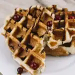 Close-up of golden Belgian waffles topped with chocolate syrup and red berries on a white plate.