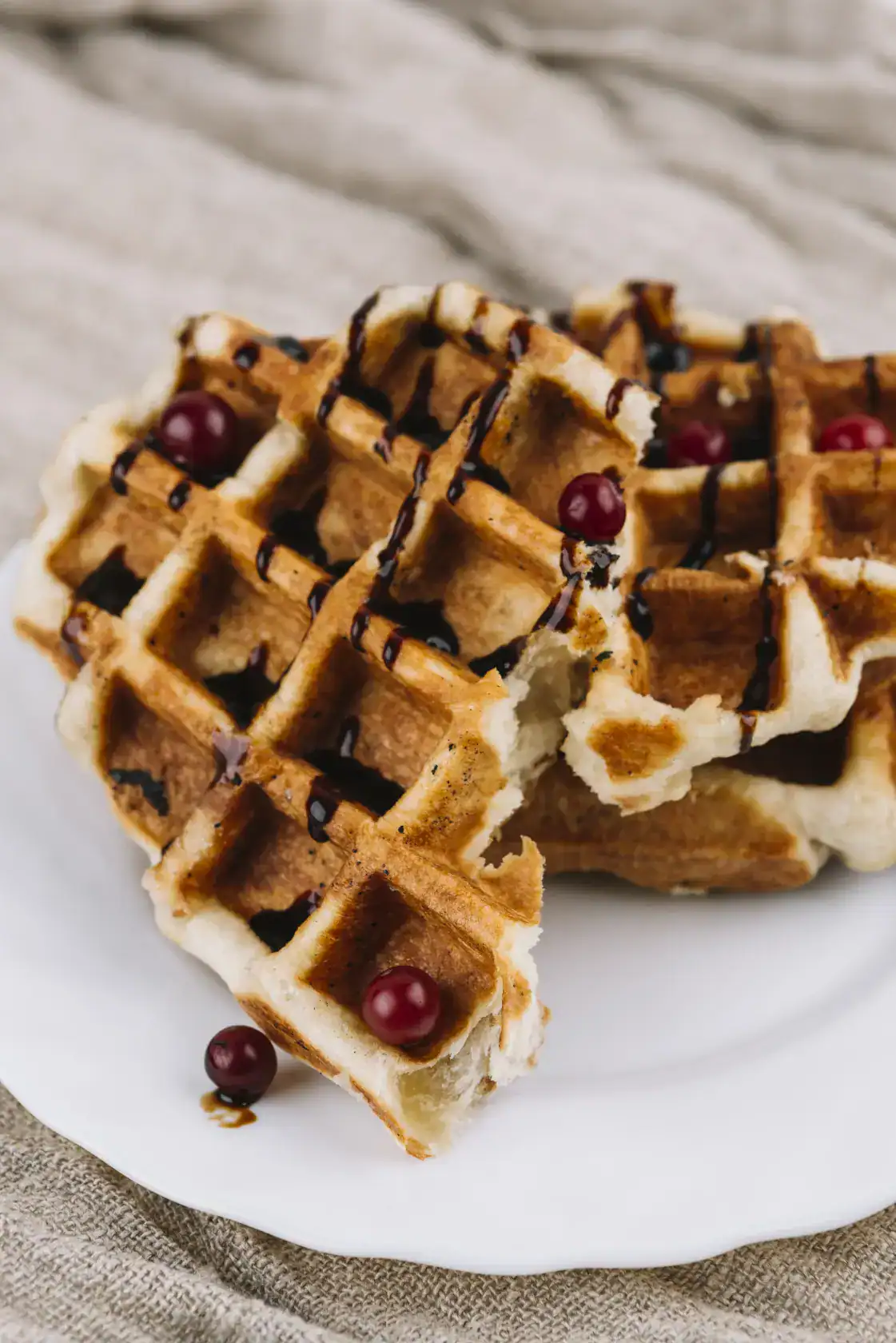 Close-up of golden Belgian waffles topped with chocolate syrup and red berries on a white plate.