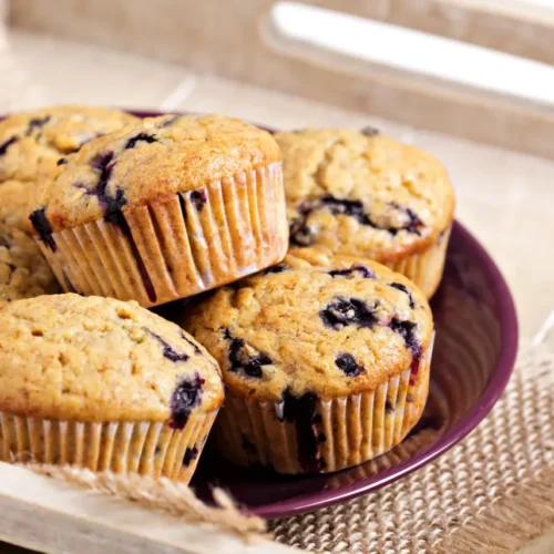 A plate of banana oatmeal muffins with blueberries, arranged on a wooden tray for a rustic presentation.