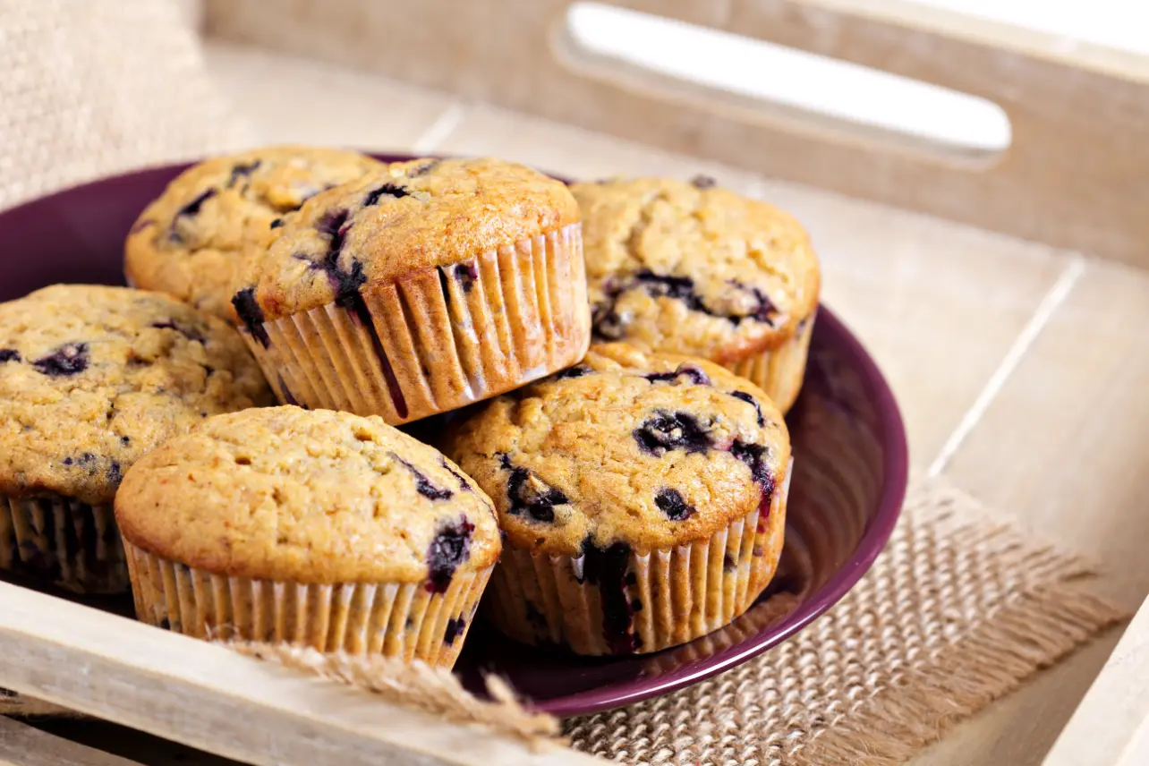 A plate of banana oatmeal muffins with blueberries, arranged on a wooden tray for a rustic presentation.