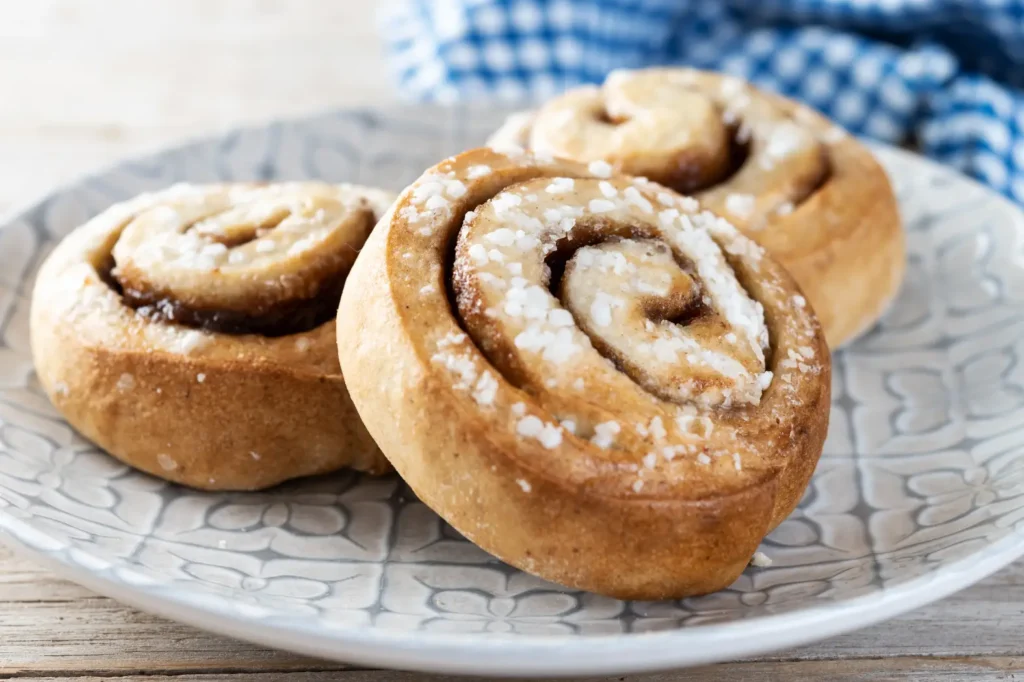 Close-up of freshly baked cinnamon rolls with sugar glaze on a patterned plate.