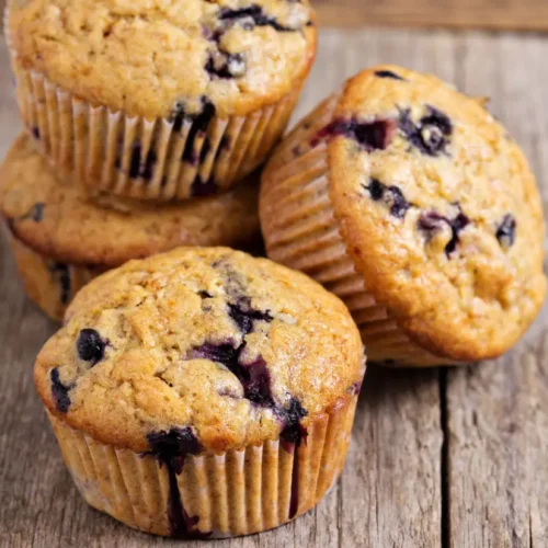 A stack of banana oatmeal muffins with blueberries on a rustic wooden surface, highlighting their golden texture and juicy filling.