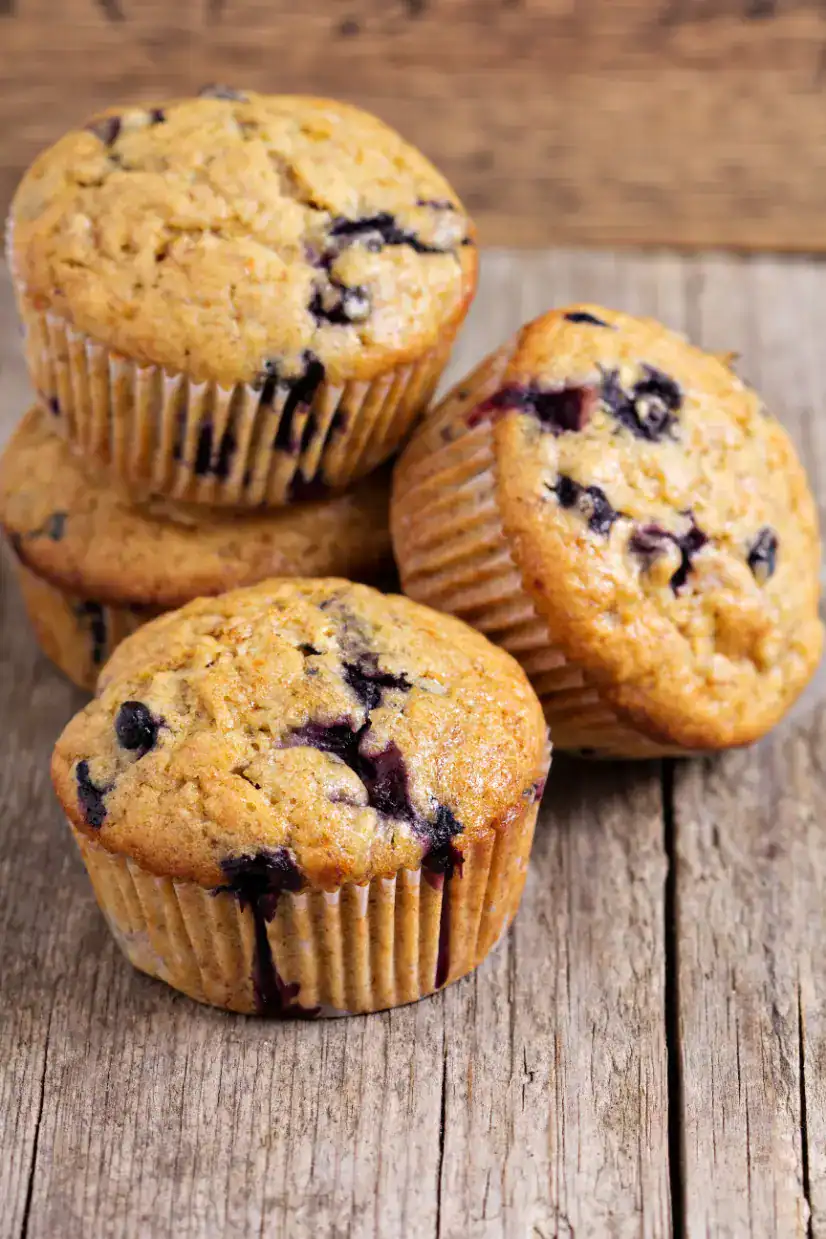 A stack of banana oatmeal muffins with blueberries on a rustic wooden surface, highlighting their golden texture and juicy filling.