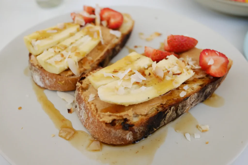 Slices of banana and strawberries on toast, topped with coconut flakes and drizzled with syrup.