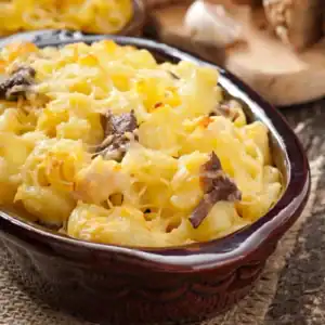 A casserole dish filled with baked mac and cheese topped with golden melted cheese and bits of mushrooms.