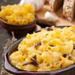 A close-up of creamy baked mac and cheese topped with melted golden cheese and mushrooms in a rustic brown dish.