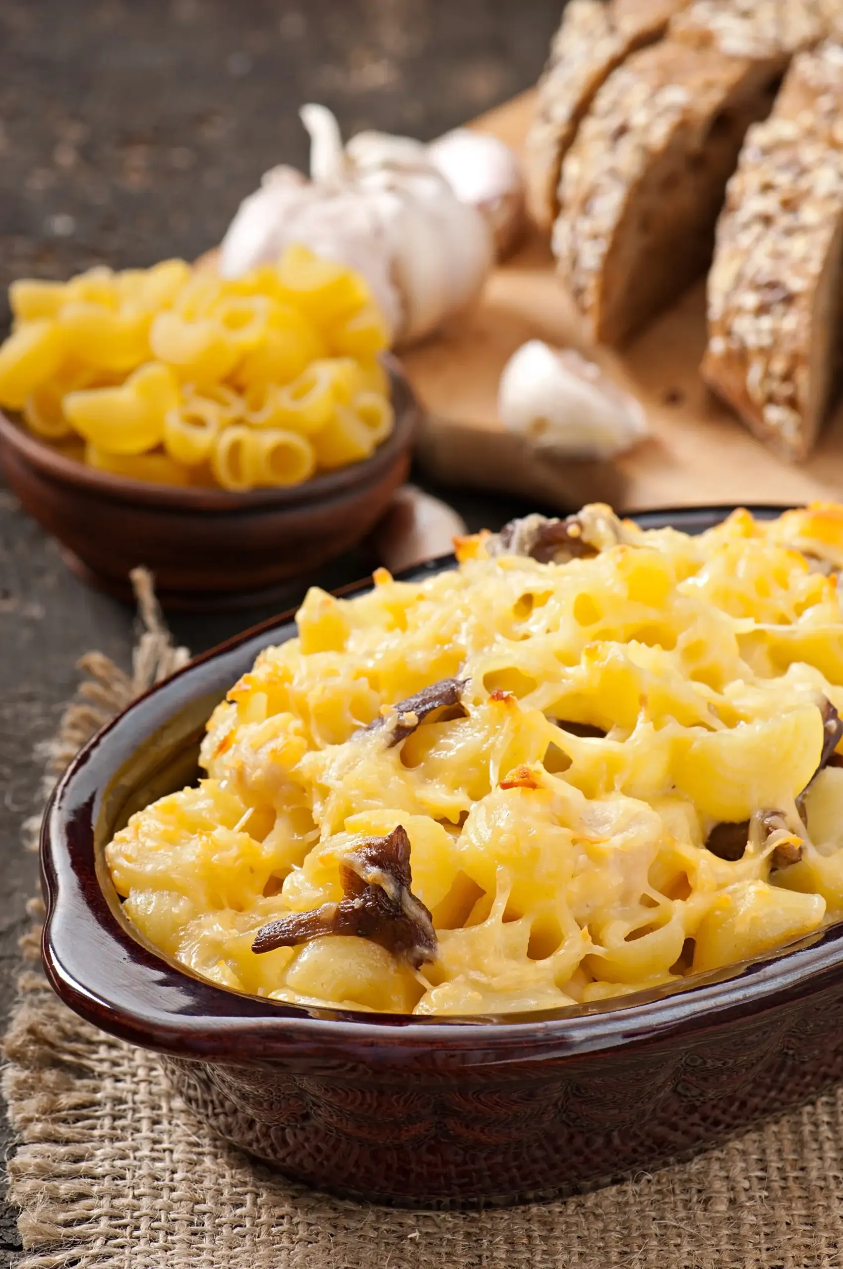 A close-up of creamy baked mac and cheese topped with melted golden cheese and mushrooms in a rustic brown dish.