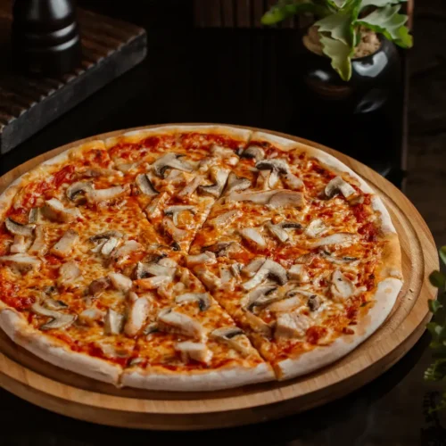 A freshly baked mushroom pizza with a thin crust, topped with melted cheese, tomato sauce, and sliced mushrooms, served on a wooden board.