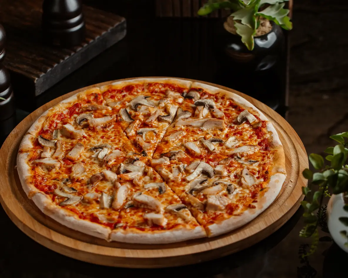 A freshly baked mushroom pizza with a thin crust, topped with melted cheese, tomato sauce, and sliced mushrooms, served on a wooden board.