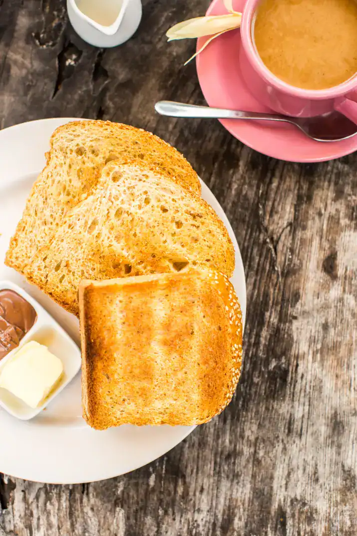 Toasted bread served with butter, chocolate paste, and a cup of coffee on the side.