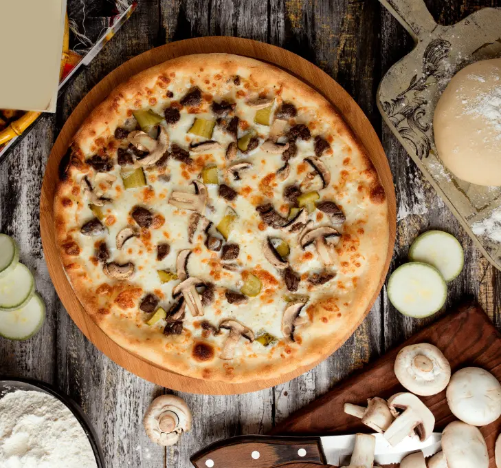 A freshly baked mushroom pizza with melted mozzarella cheese, sautéed mushrooms, diced pickles, and meat toppings, served on a wooden board surrounded by ingredients like mushrooms, zucchini, flour, and pizza dough.