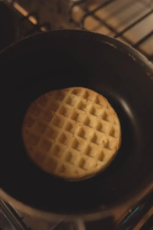 A golden waffle cooking in a pan on a stovetop, showcasing a creative method to make waffles without a waffle iron.