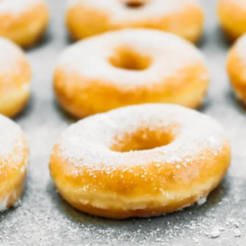 Freshly baked doughnuts dusted with powdered sugar, arranged neatly on a baking sheet. Title: How to Make Doughnuts Without Yeast – Quick and Simple Recipe