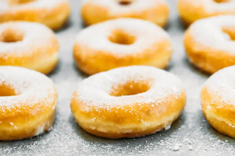 Freshly baked doughnuts dusted with powdered sugar, arranged neatly on a baking sheet. Title: How to Make Doughnuts Without Yeast – Quick and Simple Recipe