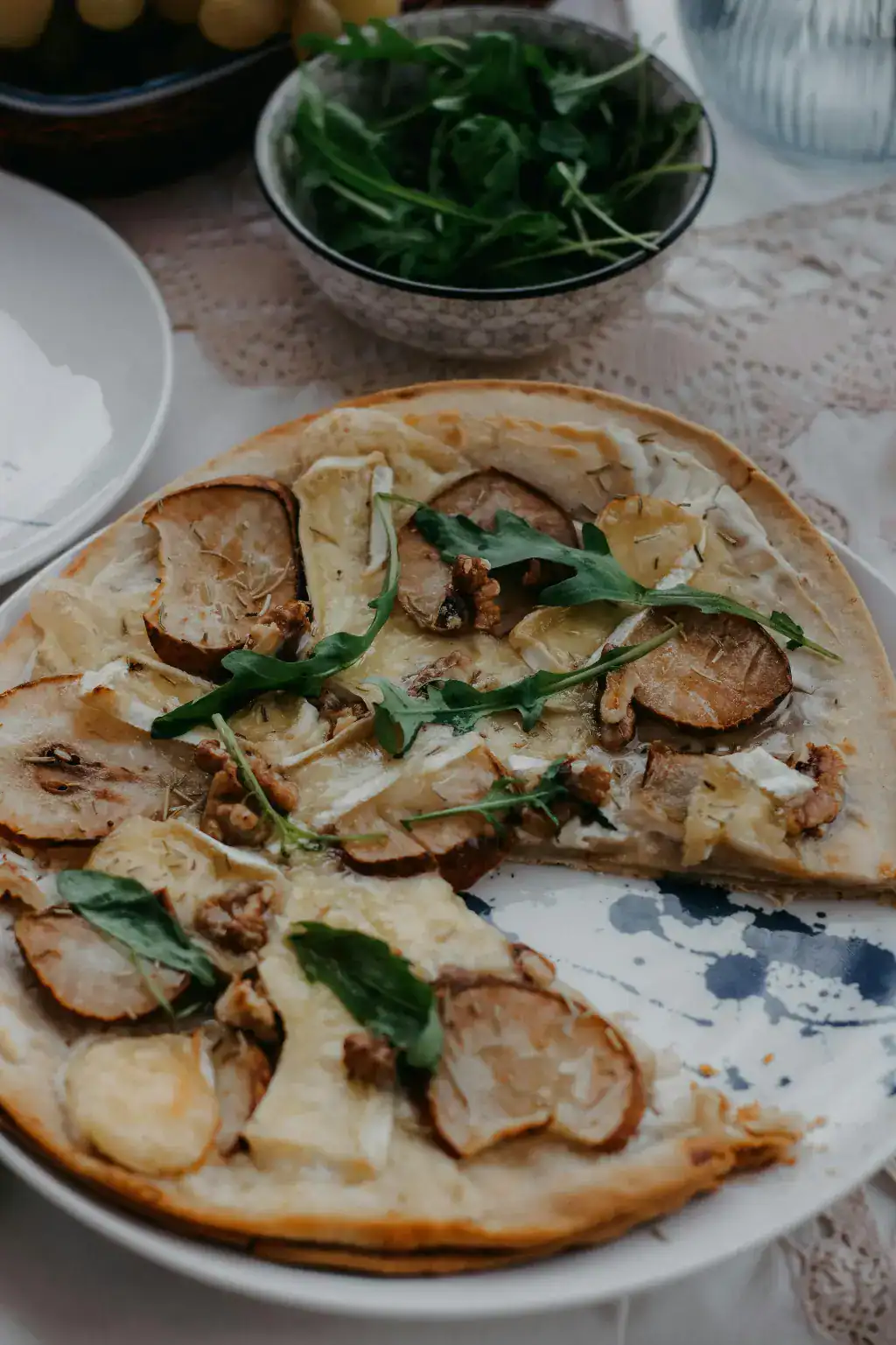 A gourmet fruit pizza topped with thinly sliced pears, melted cheese, walnuts, and fresh arugula, served on a rustic plate.