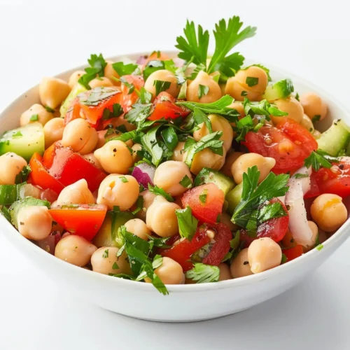 A bowl of fresh chickpea salad with chopped tomatoes, cucumbers, red onions, and parsley, dressed lightly with olive oil and herbs.