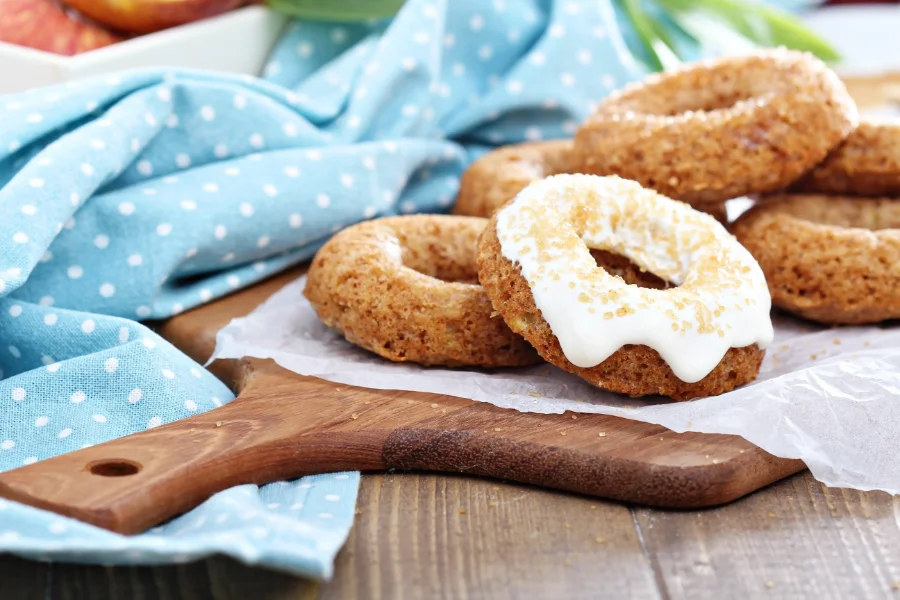 Homemade baked doughnuts without yeast, with a golden-brown crust, one topped with white glaze and sugar sprinkles, served on a wooden board.