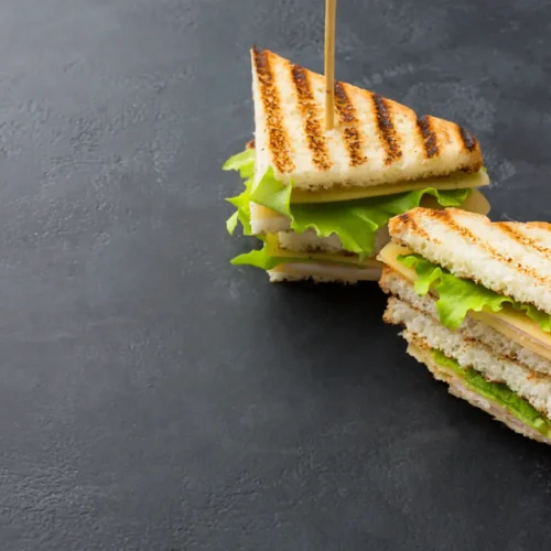 Two neatly arranged triangular club sandwiches with layers of toasted bread, lettuce, cheese, and deli meat, secured with toothpicks on a dark slate background.